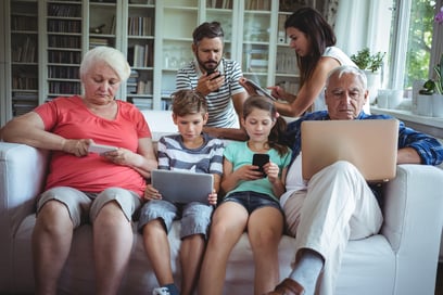 Multi-generation family sitting on sofa and using laptop, mobile phone and digital tablet